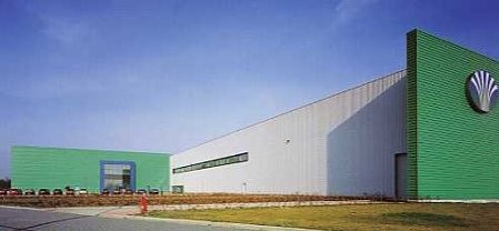 Moderne Industriehalle mit grünen Akzenten unter klarem Himmel.