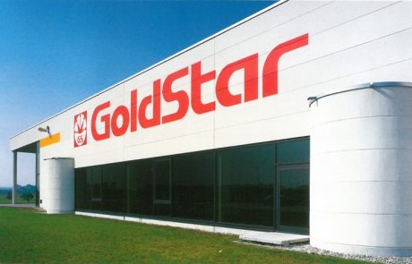 Außenansicht eines modernen Firmengebäudes mit dem Schriftzug "Goldstar" und Logo an der Fassade, große Fensterfront und blauer Himmel.