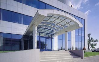Modern office building entrance with glazed façade and covered access ramp under clear skies.