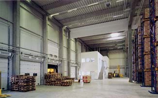 Interior view of a large warehouse with shelving systems, roller shutters and pallets of goods.