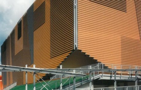 Modern building with undulating façade made of wooden slats, metal construction in the foreground.