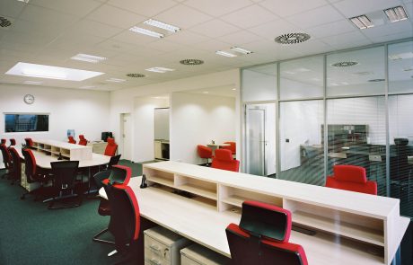 Modern office space with white tables, red chairs and glass partition walls.