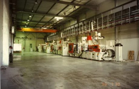 Industrial hall with machines and crane runway system with sparse lighting.