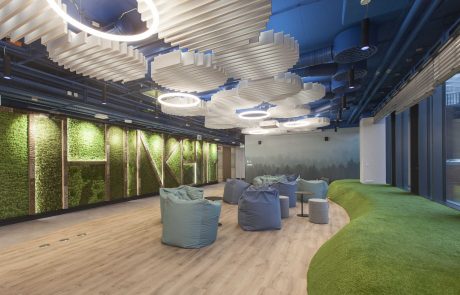 Innovatively designed office space with curved green carpet, seating areas, plant wall and wave -shaped ceiling lights.