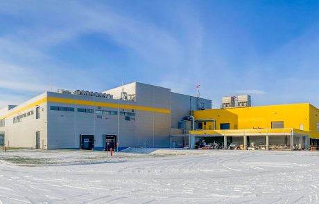 Modernes Industriegebäude mit gelber und weißer Fassade bei winterlichen Bedingungen mit Schnee auf dem Boden.