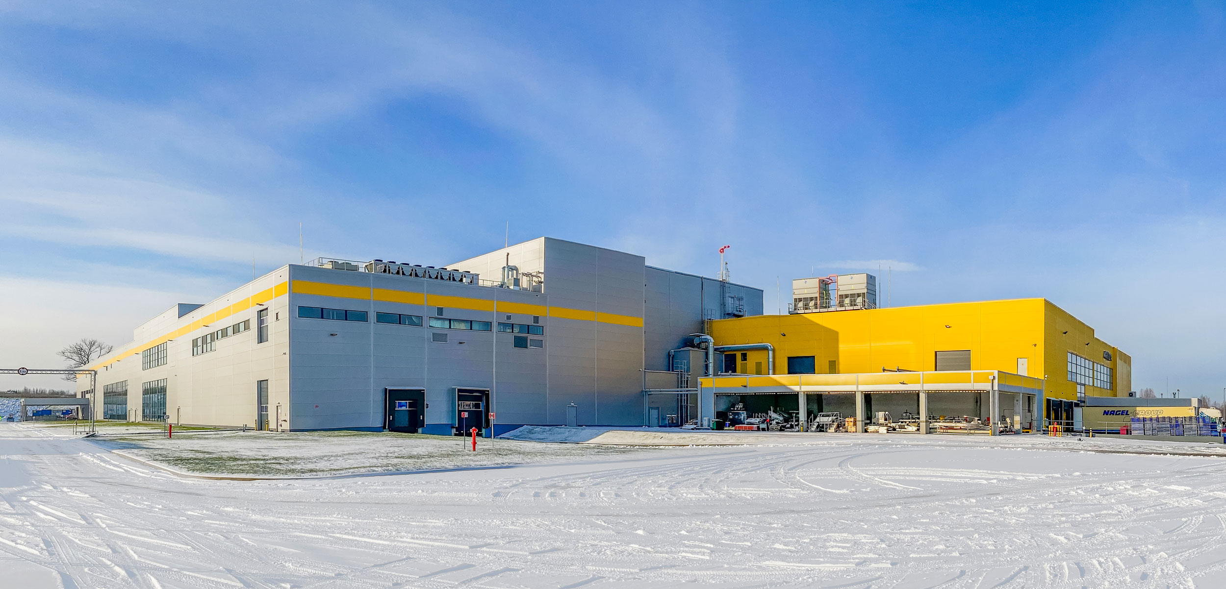 Modern industrial building with yellow and white facade in winter conditions with snow on the ground.