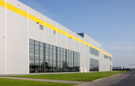 Moderne Industriehalle mit großer Glasfront und gelben Designelementen unter klarem Himmel.
