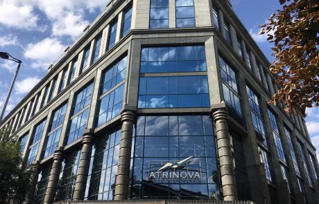Modernes Bürogebäude mit großer Glasfassade, Säulen und dem Schriftzug "ATRINOVA" unter blauem Himmel.