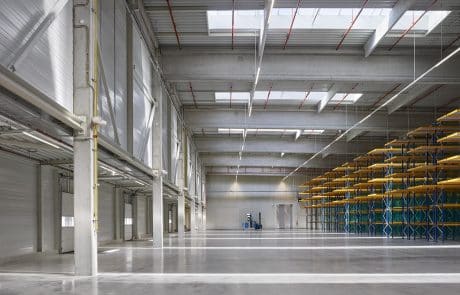 Interior view of a modern warehouse with a high ceiling, carrier structures, shelf systems and a forklift at the end of the gear.