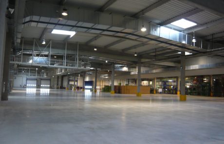 Interior view of a large, brightly lit industrial hall with steel construction and hardened soil.
