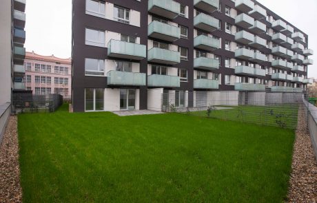 Modern apartment building with dark façade and balconies in front of a well-kept lawn.