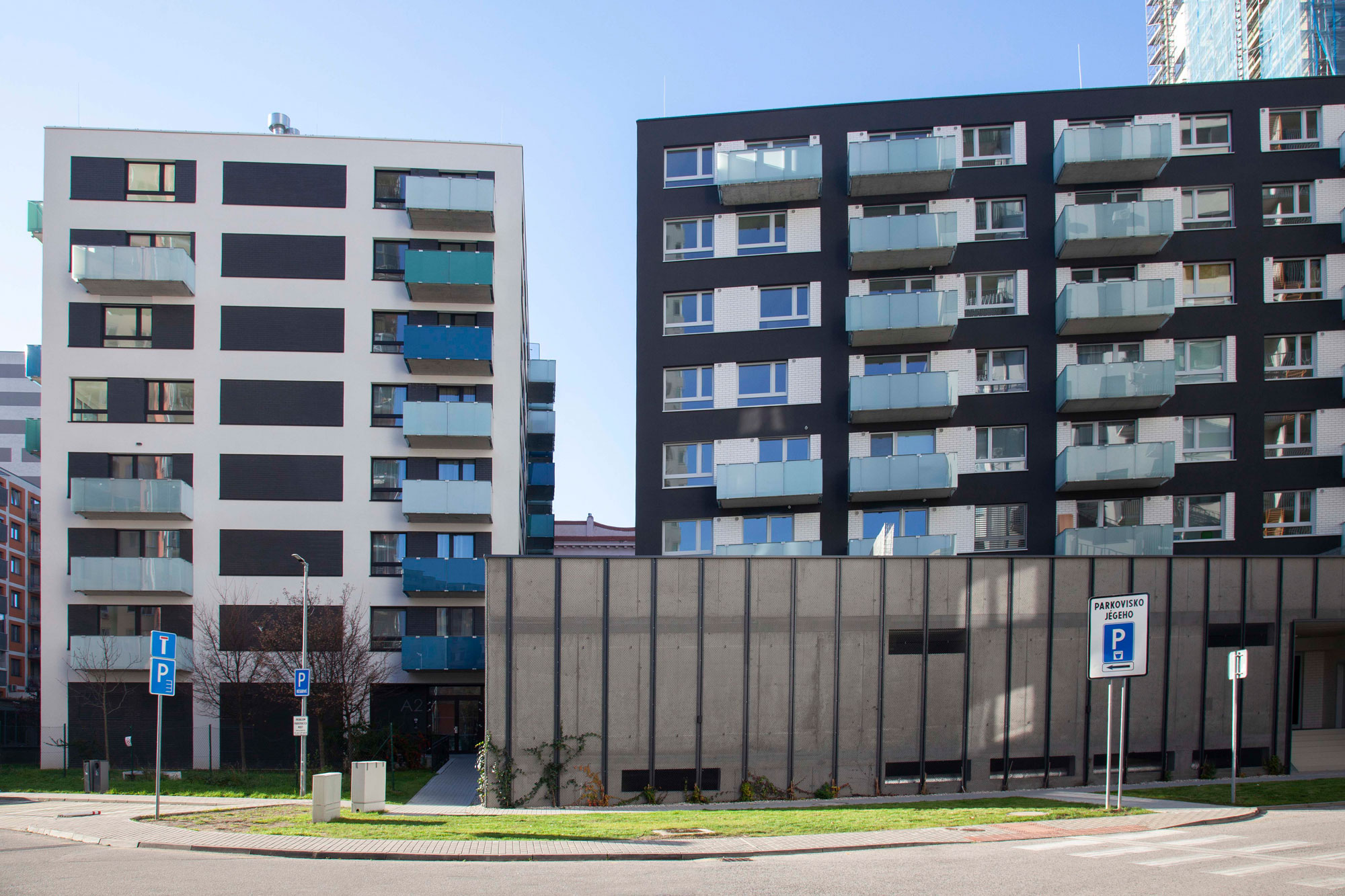 Zwei moderne Mehrfamilienhäuser mit weißen und dunklen Fassaden und Balkonen vor klarem Himmel.