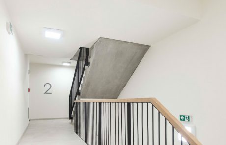 Modern staircase in a building with a white wall, black stairs and a railing made of metal rods. The number "2" on the wall indicates the floor.