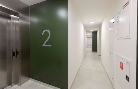 Modern hallway in a light design with numbering "2" on a green wall next to an elevator.