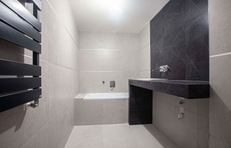 Modern bathroom with dark and light tiles, integrated bathtub and towel rail.