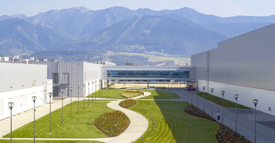 Industrial plant with well-tended green areas in the foreground and mountain backdrop in the background.