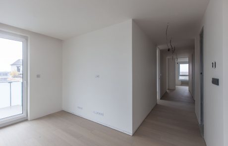 Modern empty interior of a residential building with white walls and wooden floor. The views through large windows provide a bright, inviting ambience.