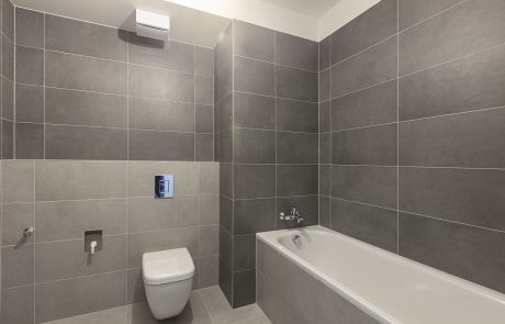 Modern bathroom interior with gray tiles on walls and floor, built-in bathtub, wall-mounted toilet and washbasin.