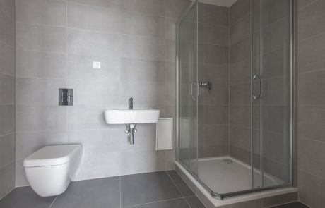 Modern bathroom interior with gray tiles, glass shower cubicle, wall-mounted sink and hanging toilet.