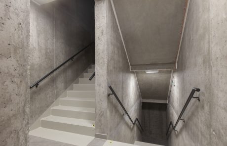 Modern staircase in a building, designed with concrete walls and white steps. Elegant, minimalist design with black handrails and selective lighting.