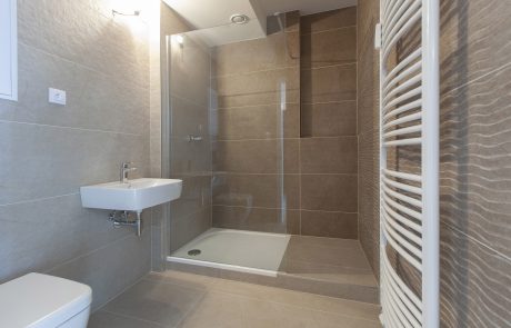 Modern bathroom with a large shower with a glass partition, beige wall tiles, a white wall-mounted washbasin and a towel rail in a radiator design.