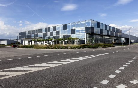 Modern office building with reflective glass facades and clear lines, surrounded by green outdoor areas. Large lettering "InoBat" on the front.