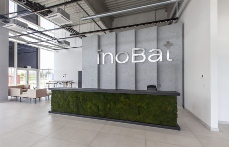 Modern entrance hall with minimalist reception, accent wall and integrated moss design, open ceiling construction in industrial style. Text at reception reads "inoBa".