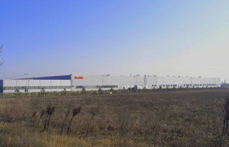 Large industrial building with Makita logo under a blue sky, surrounded by dry grassland.