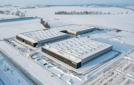 Aerial view of a large industrial complex in winter with snow-covered roofs and surrounding snowy landscape.