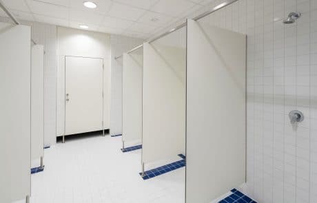 Innenansicht eines sauberen, hellen Duschraums mit weißen Kacheln und Trennwänden sowie blauen Bodenfliesen.