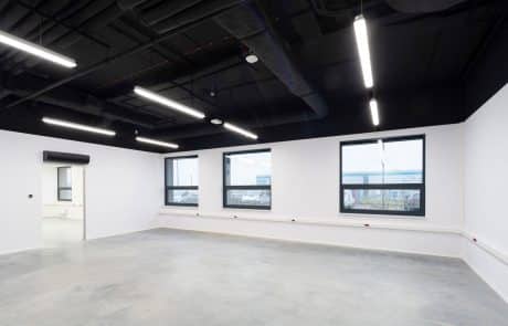 Interior view of an empty, bright office space with a concrete floor, white walls and four windows.