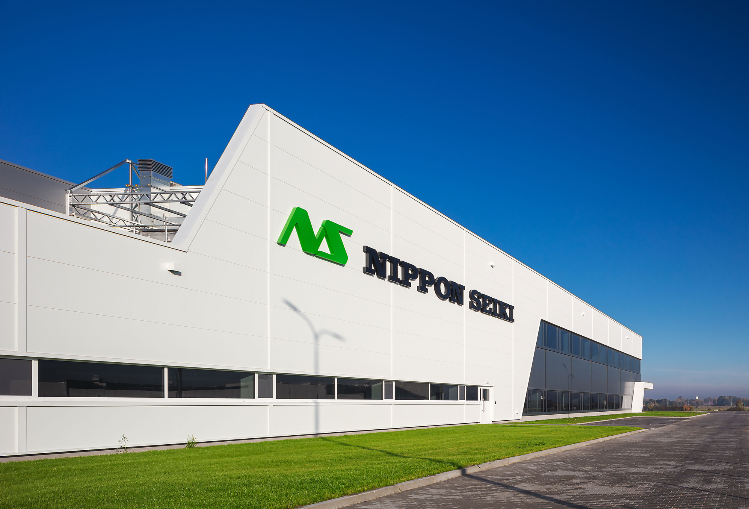 Moderne Firmenfassade von Nippon Seiki mit großem Logo unter blauem Himmel, umgeben von einer gepflegten Grünfläche.