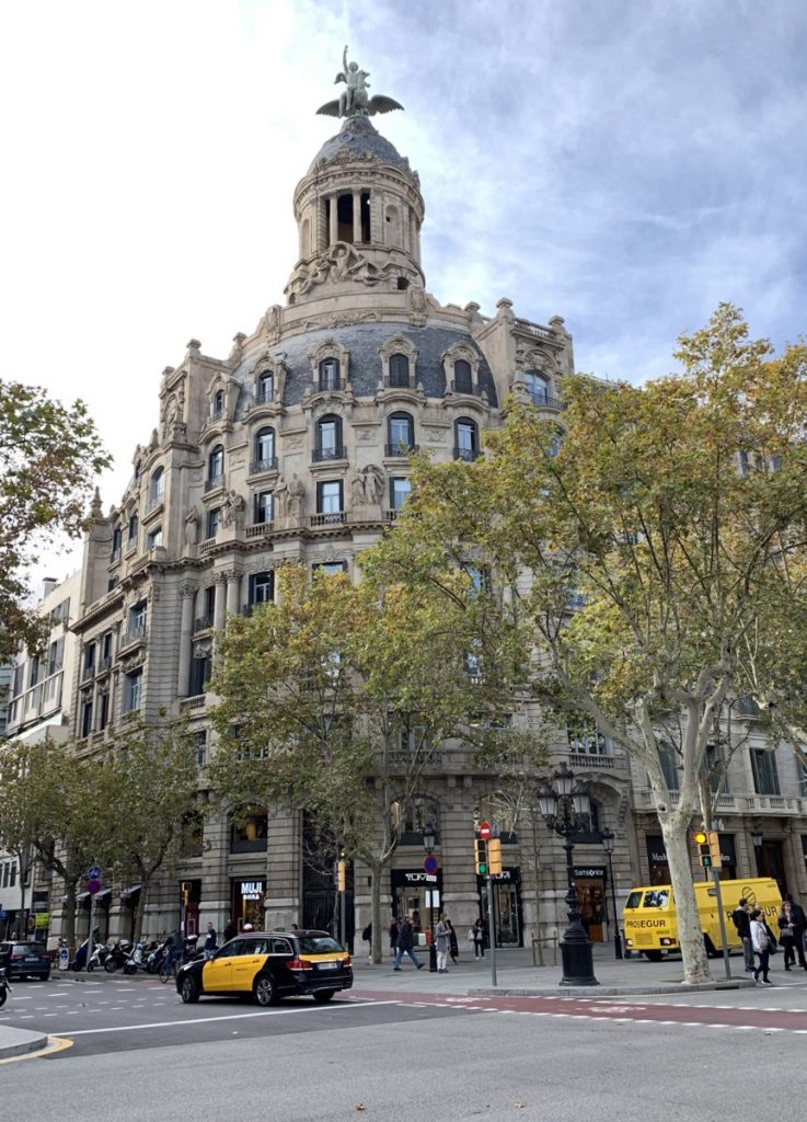 Baroque-inspired building on a busy street with a sculptural rooftop and autumn trees.