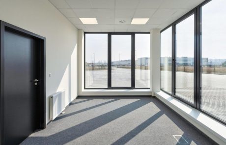 Empty office space with large windows that let in daylight and a view of an outdoor area.