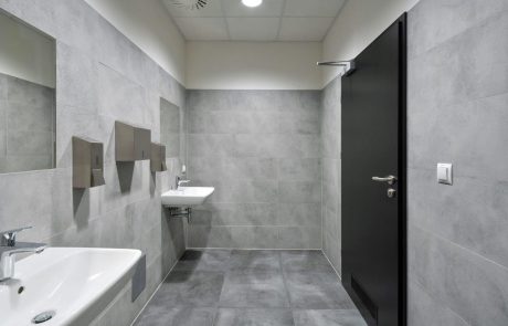 Modernes Badezimmer mit grauen Fliesen, ausgestattet mit Waschbecken, Spiegel und geschlossener schwarzer Tür.