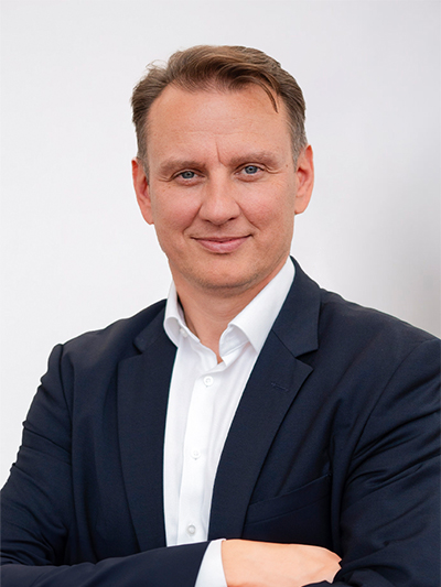 Porträt eines lächelnden Mannes (Mr. Koljadenk) mit Anzug und weißem Hemd vor einem weißen Hintergrund.