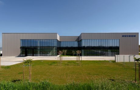 Modern industrial architecture: building with a metal facade, large window fronts and clear lines, surrounded by green.