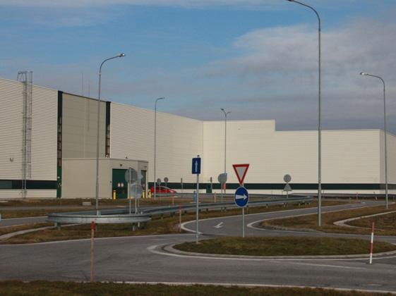 Außenansicht einer PSA Peugeot Citroën Fabrik mit weißen Fassaden, Straßenschildern und einem Kreisverkehr.